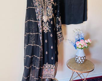 May include: A black three-piece outfit with intricate embroidery. The outfit includes a long-sleeved top, trousers, and a sheer dupatta. The dupatta has a silver border and is draped over a mannequin.