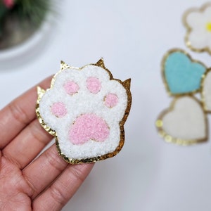 May include: A white and pink fuzzy paw print with gold glitter trim. The paw print is a craft supply for making hair bows, headbands, and other accessories.