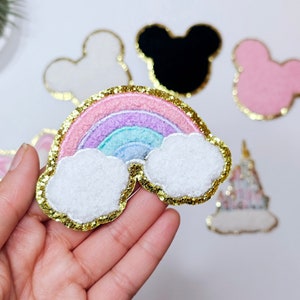 May include: A rainbow-colored felt patch with gold glitter trim and two white fluffy clouds. The patch is perfect for adding a whimsical touch to clothing, bags, or other crafts.