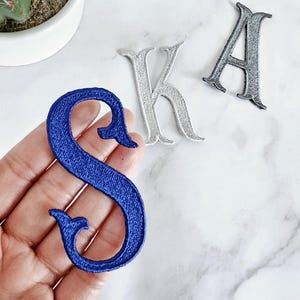 Puede incluir: Tres parches bordados para planchar en forma de las letras S, K y A. La S es azul, la K es blanca y la A es gris.