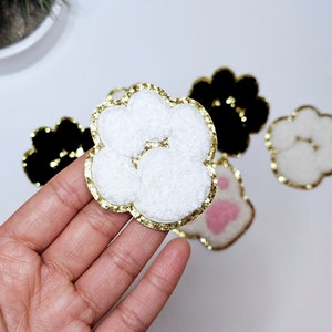 May include: A set of five paw print iron-on patches. The patches are in various colors and styles, including black, white, pink, and gold. The patches are perfect for adding a touch of personality to clothing, bags, or other accessories.
