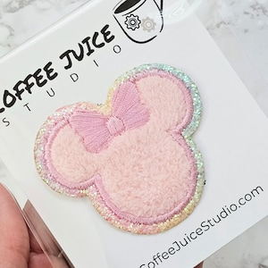 May include: Pink fuzzy Minnie Mouse head shaped patch with a pink bow and iridescent glitter trim. The patch is on a white background with the text "Coffee Juice Studio" in the bottom right corner.