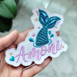 May include: White iron-on patch with a pink embroidered name "Amori" and a blue and green mermaid tail with iridescent scales.
