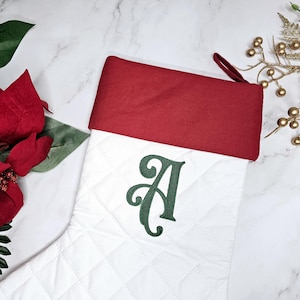 May include: White quilted Christmas stocking with a red cuff and a green embroidered letter A.