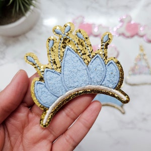 May include: A blue and gold glitter crown with a scalloped edge. The crown is made of felt and has a gold glitter trim.