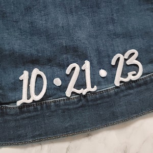 May include: A close-up of a denim jacket with a white embroidered patch that says "10.21.23".