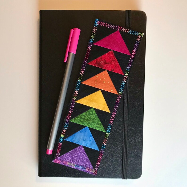 May include: A black leather journal with a rainbow fabric bookmark. The bookmark is made of sewn triangles in a rainbow pattern.