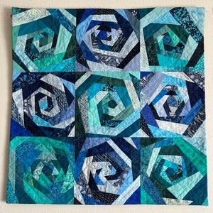 May include: A quilt featuring a repeating pattern of blue and green spiral designs. The quilt is crafted from various shades of blue and green fabric, with the spirals formed by piecing together different fabric scraps.