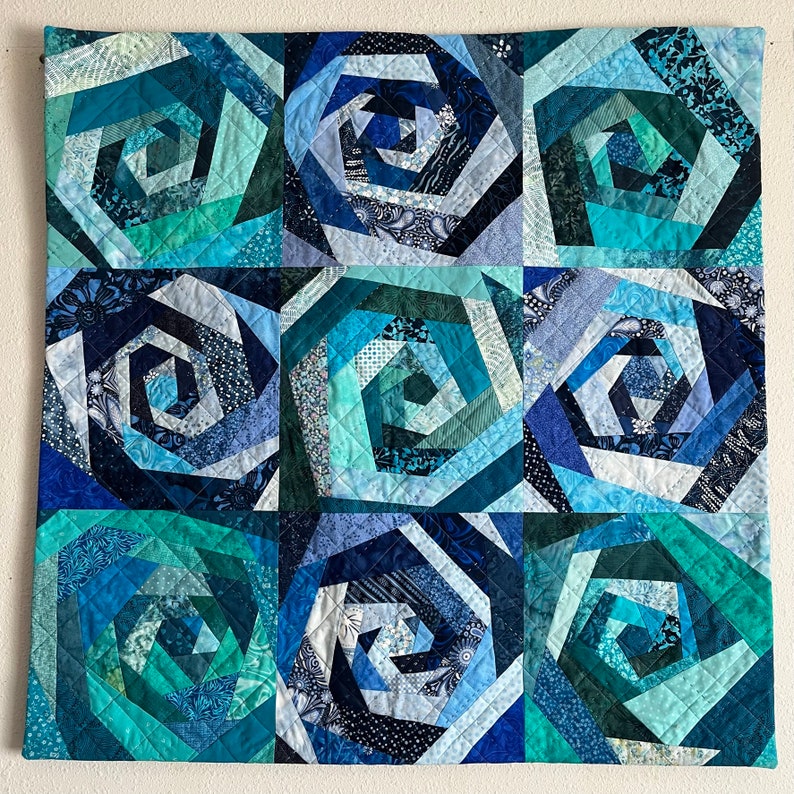 May include: A quilt featuring a repeating pattern of blue and green spiral designs. The quilt is crafted from various shades of blue and green fabric, with the spirals formed by piecing together different fabric scraps.