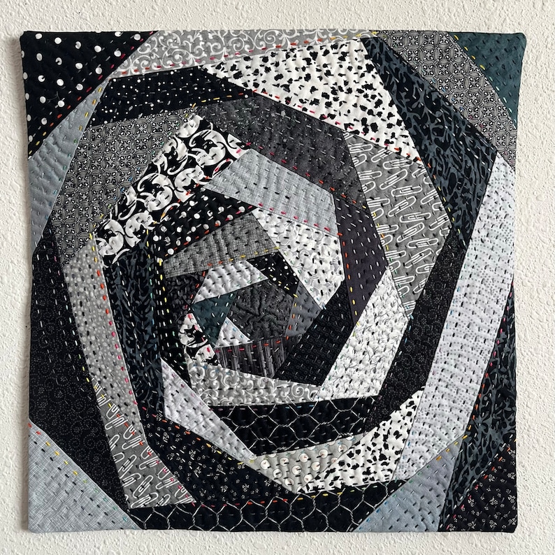 May include: A black and white quilt with a spiral pattern. The quilt is made of different fabrics with various textures and patterns. The quilt is stitched together with black thread.