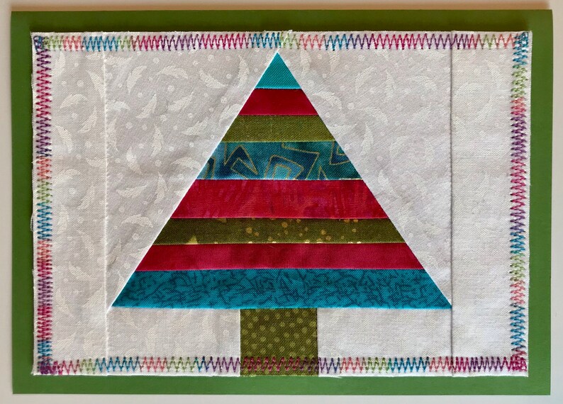 May include: A colorful patchwork Christmas tree made of fabric scraps. The tree is layered with red, green, blue, and gold fabric. The tree is surrounded by a white background with a subtle pattern.