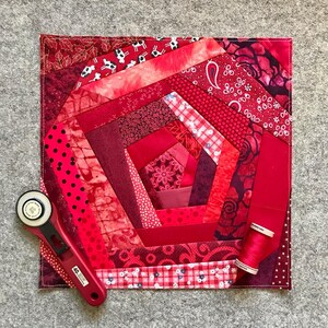 May include: A red and white quilt with a spiral pattern. The quilt is made of various fabrics with different patterns and textures. The quilt is surrounded by a white border.