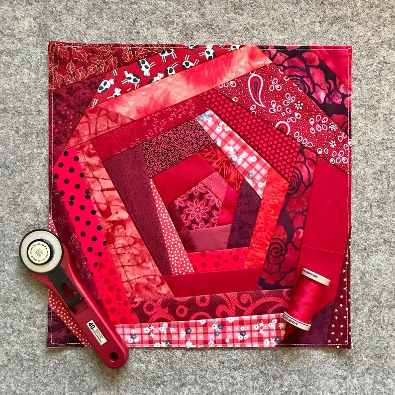 May include: A red and white quilt with a spiral pattern. The quilt is made of various fabrics with different patterns and textures. The quilt is surrounded by a white border.