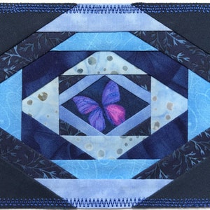 May include: A blue and purple quilt block with a butterfly design in the center. The quilt block is made of various shades of blue fabric and has a dark blue border.