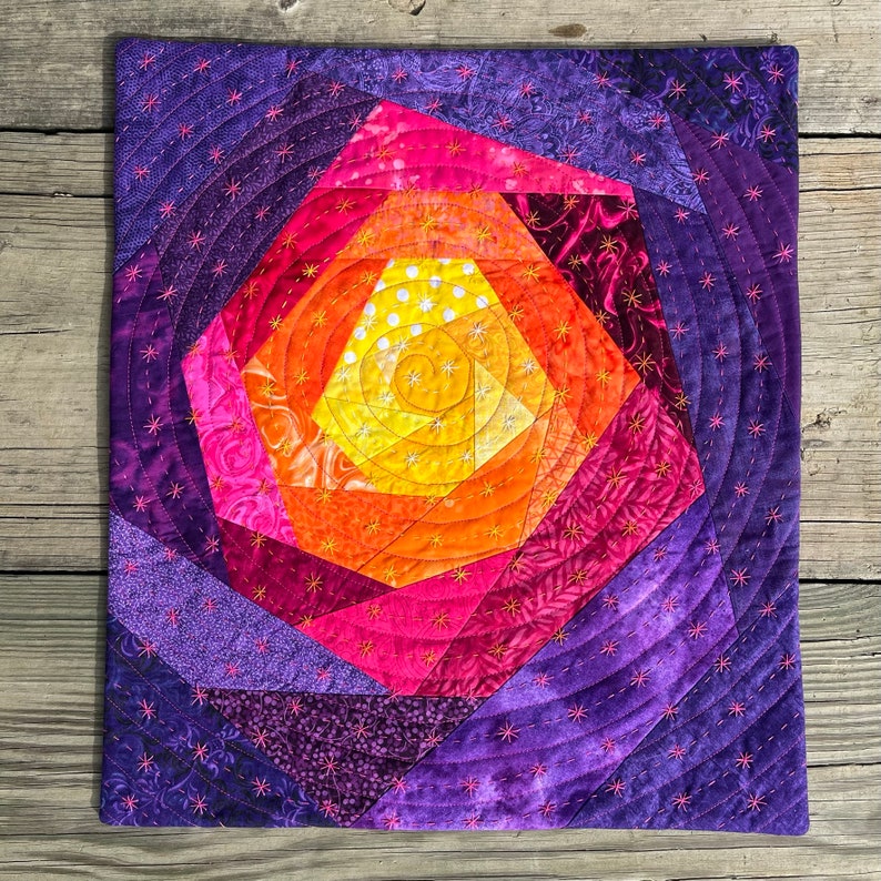 May include: A purple, pink and orange quilt with a spiral design. The quilt is made of fabric scraps and is quilted with a star-shaped stitch.