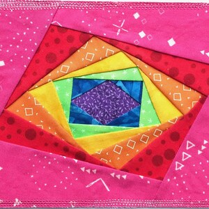 May include: A colorful rainbow quilt block with a spiral design. The center of the block is a purple and blue diamond shape surrounded by green, yellow, orange, and red fabric.