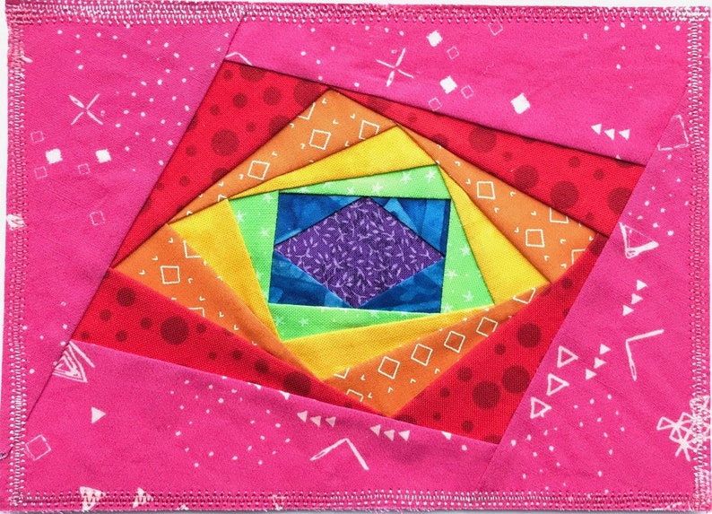 May include: A colorful rainbow quilt block with a spiral design. The center of the block is a purple and blue diamond shape surrounded by green, yellow, orange, and red fabric.