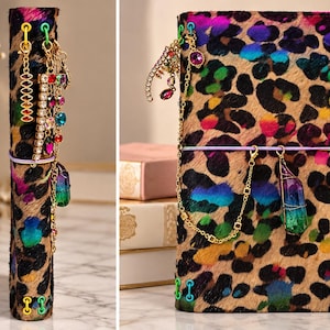 May include: A journal with a textured leopard print cover featuring vibrant neon blue, pink, and green patches. The spine and cover are adorned with gold-toned metal chains, colorful crystal charms, and a large iridescent crystal pendant.