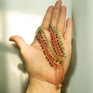 Peut inclure: Cinq bracelets en cha&icirc;ne dor&eacute;e avec des perles color&eacute;es. Les bracelets sont superpos&eacute;s et ont de petits pendentifs dor&eacute;s &agrave; l'extr&eacute;mit&eacute;.