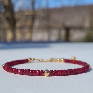 Peut inclure: Un bracelet en pierres précieuses rouges avec des perles dorées. Le bracelet est composé de petites pierres précieuses rouges facettées et présente un design simple et élégant.