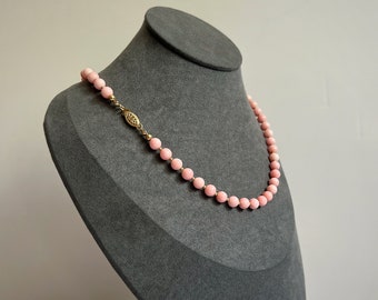 May include: A pink coral bead necklace with a gold clasp on a gray jewelry display stand.