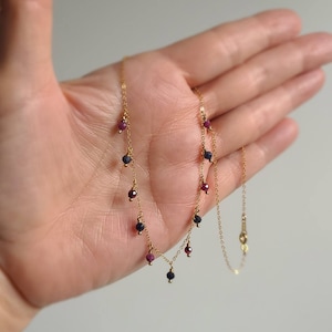 Può includere: Una collana a catena d'oro con pietre preziose rosse e blu pendenti.