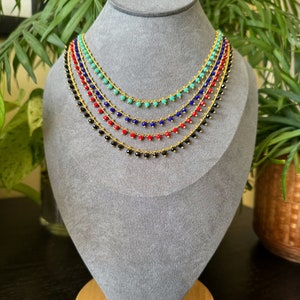 Peut inclure: Cinq colliers superpos&eacute;s avec des cha&icirc;nes dor&eacute;es et de petites perles. Les perles sont noires, rouges, bleues et turquoise.