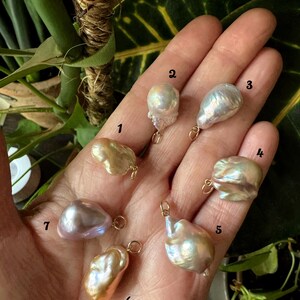 以下が含まれることがあります： 金色のループが付いた、形が不規則で虹色の7つのバロックパールのコレクション。 パールはクリーム、ピーチ、ラベンダーの色合いなど、さまざまな色があります。 パールはニュートラルな背景に表示され、そのユニークな形と色を際立たせています。