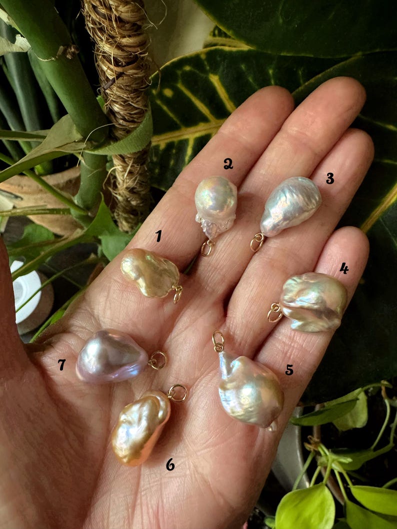 以下が含まれることがあります： 金色のループが付いた、形が不規則で虹色の7つのバロックパールのコレクション。 パールはクリーム、ピーチ、ラベンダーの色合いなど、さまざまな色があります。 パールはニュートラルな背景に表示され、そのユニークな形と色を際立たせています。