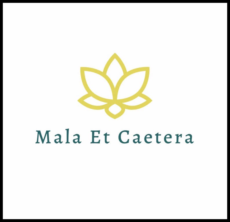 以下が含まれることがあります： 水色の文字「Mala Et Caetera」の上に、金の蓮の花のデザインが施されたロゴ。ロゴは黒い縁取りのある白い背景に配置されています。