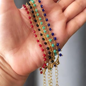 Peut inclure: Cinq bracelets en cha&icirc;ne dor&eacute;e avec de petites perles color&eacute;es. Les bracelets sont rouge, noir, turquoise, bleu et noir. Les bracelets ont un fermoir dor&eacute; et un petit charme dor&eacute;.