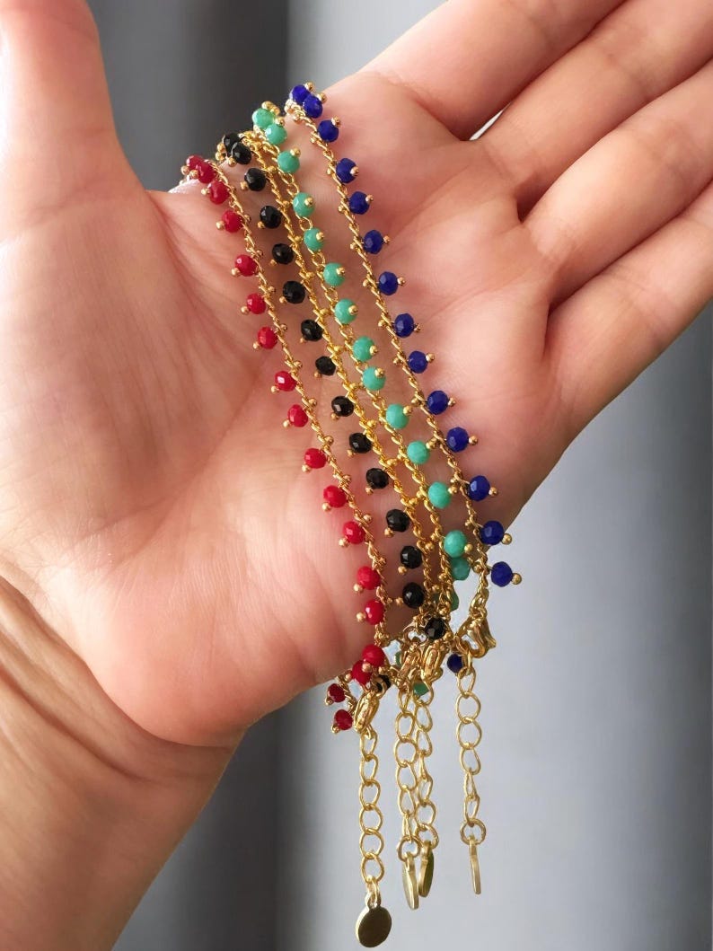 Peut inclure: Cinq bracelets en cha&icirc;ne dor&eacute;e avec de petites perles color&eacute;es. Les bracelets sont rouge, noir, turquoise, bleu et noir. Les bracelets ont un fermoir dor&eacute; et un petit charme dor&eacute;.
