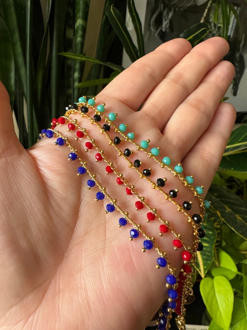 Peut inclure: Cinq cha&icirc;nes dor&eacute;es avec des perles pendantes turquoise, noires, rouges et bleues.