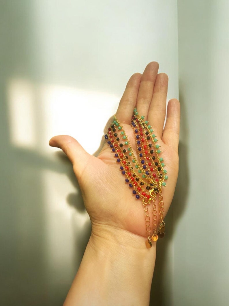 Peut inclure: Cinq bracelets en cha&icirc;ne dor&eacute;e avec des perles color&eacute;es. Les bracelets sont superpos&eacute;s et ont de petits pendentifs dor&eacute;s &agrave; l'extr&eacute;mit&eacute;.