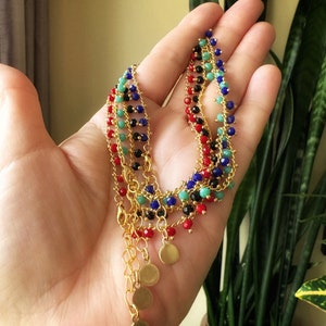 Peut inclure: Un ensemble de quatre colliers en cha&icirc;ne dor&eacute;e avec des perles color&eacute;es. Chaque collier a une couleur de perles diff&eacute;rente&nbsp;: rouge, noir, bleu et vert. Les colliers ont des breloques en forme de disque dor&eacute;s aux extr&eacute;mit&eacute;s.