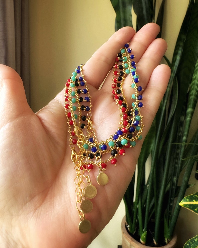 Peut inclure: Un ensemble de quatre colliers en cha&icirc;ne dor&eacute;e avec des perles color&eacute;es. Chaque collier a une couleur de perles diff&eacute;rente&nbsp;: rouge, noir, bleu et vert. Les colliers ont des breloques en forme de disque dor&eacute;s aux extr&eacute;mit&eacute;s.