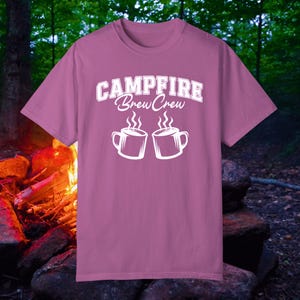 May include: A pink t-shirt with the text "Campfire Brew Crew" in white. Two white mugs with steam coming out of them are below the text.