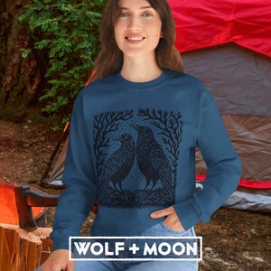 May include: A dark blue sweatshirt with a black and white illustration of three birds in a forest setting. The text "WOLF + MOON" is printed on the bottom of the sweatshirt.