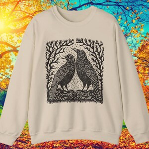 May include: A cream-colored sweatshirt with a black and white illustration of two crows perched on branches. The illustration is in a woodcut style.