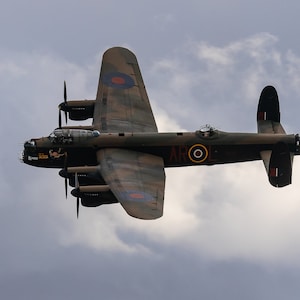 Pode incluir: Um avião bombardeiro vintage verde escuro e marrom com círculos vermelhos, brancos e azuis voando em um céu nublado. O avião tem a palavra "AROL" escrita no lado.