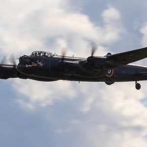 May include: A black Avro Lancaster bomber aircraft flies against a cloudy sky. The aircraft has a pink nose art design and the text "F-for Freddie" on the side.
