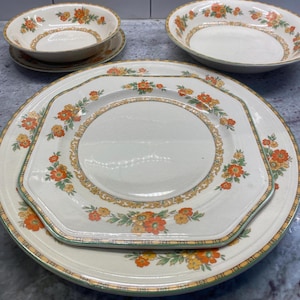 May include: A collection of vintage cream-colored ceramic dishware with orange and yellow floral patterns. The set includes plates, bowls, and saucers. The plates have a unique octagonal shape, and the rims are trimmed with a green border.
