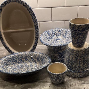 May include: A collection of blue and white spatterware pottery. The set includes an oval divided serving dish, a round bowl, a pedestal bowl, a small cup, and two flower pots. The pottery has a speckled design.