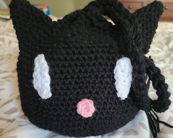 May include: Black crocheted cat-shaped drawstring bag with white eyes and a pink nose.