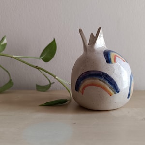 May include: A white ceramic pomegranate vase with a speckled glaze and painted rainbow designs.
