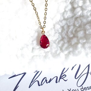 May include: A gold chain necklace with a teardrop-shaped red gemstone pendant.