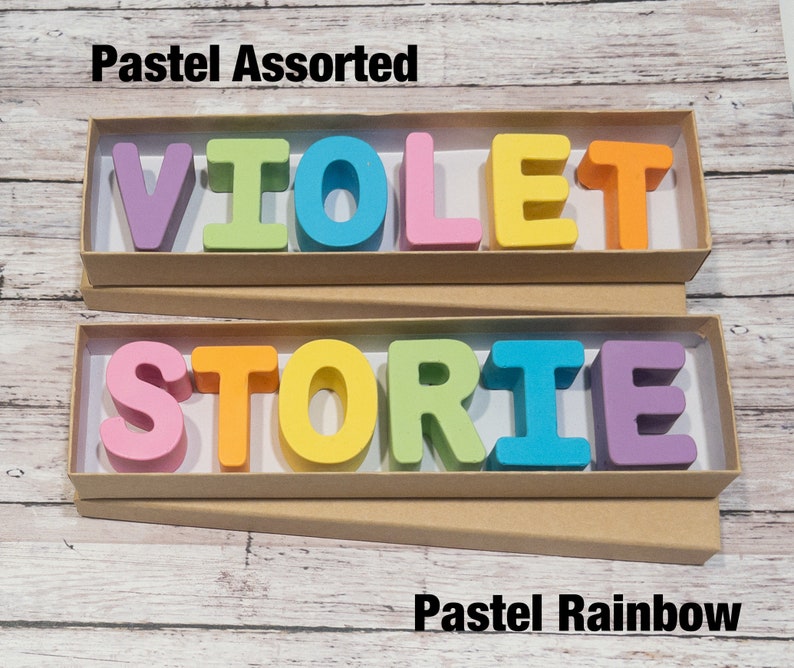 May include: Two boxes of wooden letters spelling out the words "VIOLET" and "STORIE". The letters are in pastel colors, with the top box labeled "Pastel Assorted" and the bottom box labeled "Pastel Rainbow".