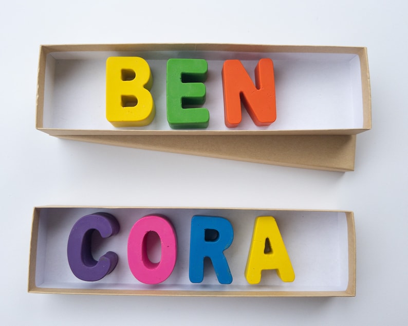 May include: Two boxes with the names "BEN" and "CORA" spelled out in colorful letters. The letters are made of wax and are arranged in the boxes.