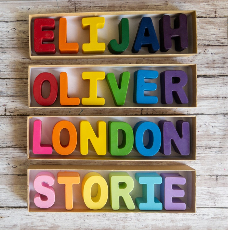 May include: Four boxes with rainbow colored letters spelling out the names Elijah, Oliver, London, and Storie. The letters are made of wax and are arranged in a row in each box.