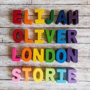 May include: Colorful wooden letter blocks spelling out the names Elijah, Oliver, London, and Storie on a white wood background.